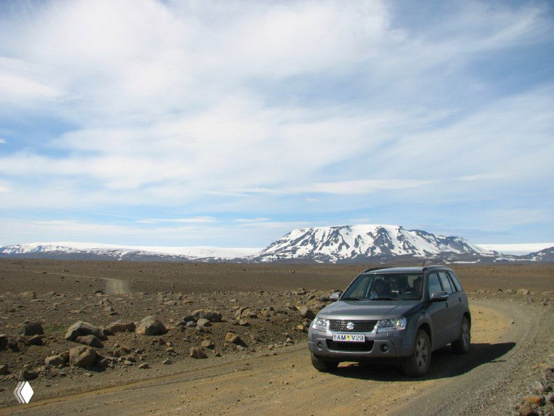 Серый внедорожник едет по гравийной дороге на фоне равнины и заснеженных гор, иллюстрация условий для автомобилного маршрута по Исландии.