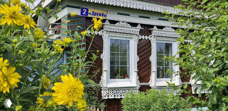 Уютный деревянный дом с белой резной отделкой наличников и яркими цветами на переднем плане — патриархальная архитектура Боровска.