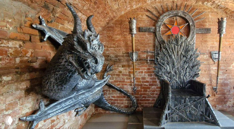 Интерьер музейной экспозиции с крупными арт-объектами: скульптура дракона и трон в стиле «Игры престолов», индустриальная подсветка.