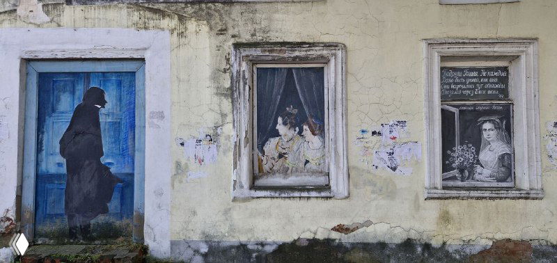 Ряд настенных картин, выполненных как «окна»: силуэты, сцены и портреты в разной технике на фасаде старого дома
