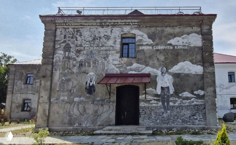 Монументальная монохромная роспись фасада: фигура человека на фоне облаков и текстовые фрагменты, крупный масштаб и сдержанная палитра