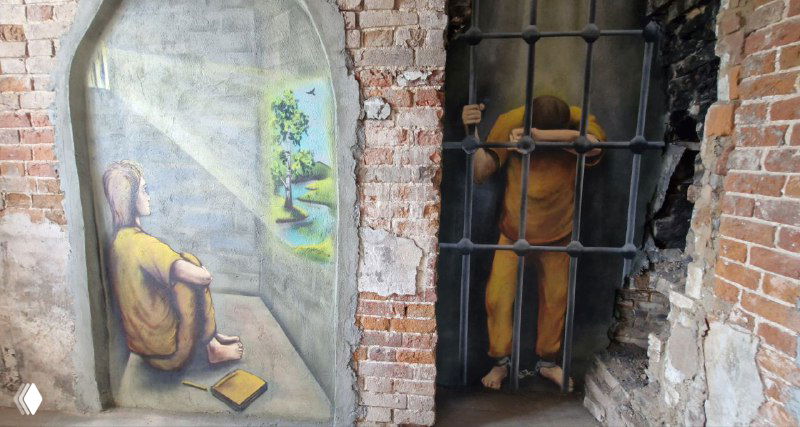 Росписи в кирпичной арке и нишах: сцена с сидящим человеком и фигурой за решёткой, яркое сочетание света и тени в городской среде