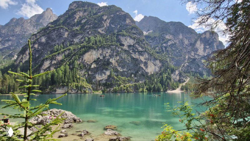 Панорамный вид озера Брайес: бирюзовая вода, каменистый берег и крутые скальные стены Доломитов на заднем плане.