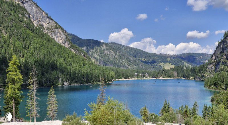 Озеро Брайес в голубых тонах, окрестные леса и хребты Доломитов, вид с противоположного берега на спокойную воду.