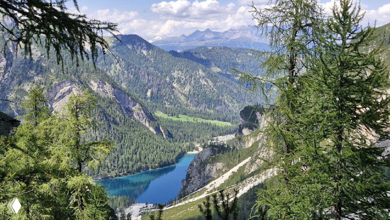 Бирюзовая вода между лесистыми склонами; вид сверху на озеро и извилистую дорогу у его берегов в долине Доломитов.