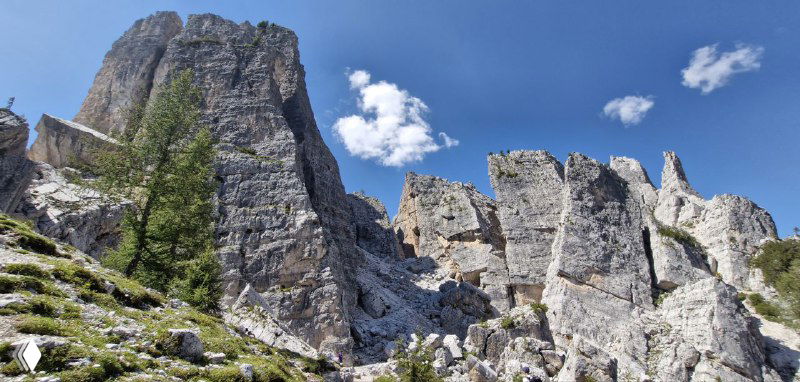 Крупный план отвесных каменных стен Cinque Torri: серые карнизы, трещины и облака на фоне горного неба.