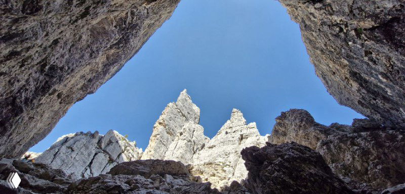 Вид из узкого прохода-пещеры внутрь массива: силуэты зазубренных вершин и синий окаймлённый небом промежуток в центре кадра.
