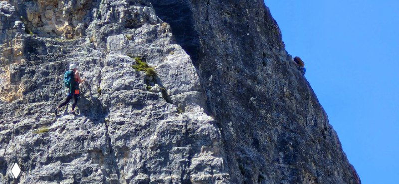 Скалолаз в снаряжении на вертикальной стене Cinque Torri; акцент на людях, которые выбираются вверх по гладким скалам.