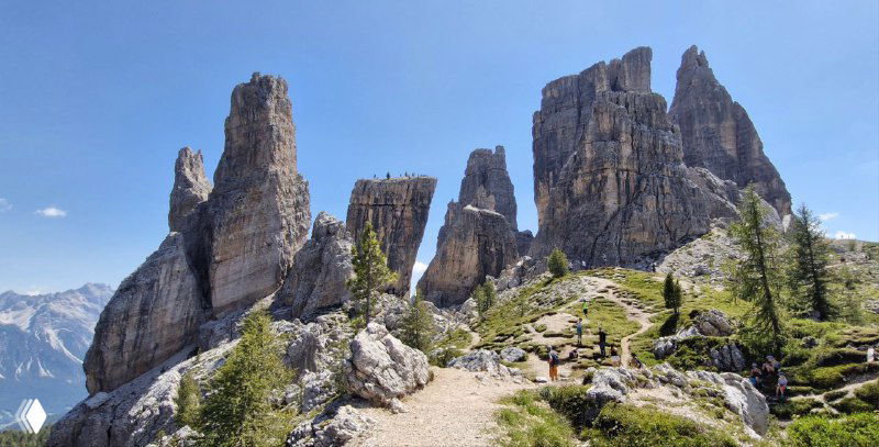 Тропа и туристы вокруг характерных столбов Cinque Torri; панорамный вид верховых маршрутов и каменистых формирований.