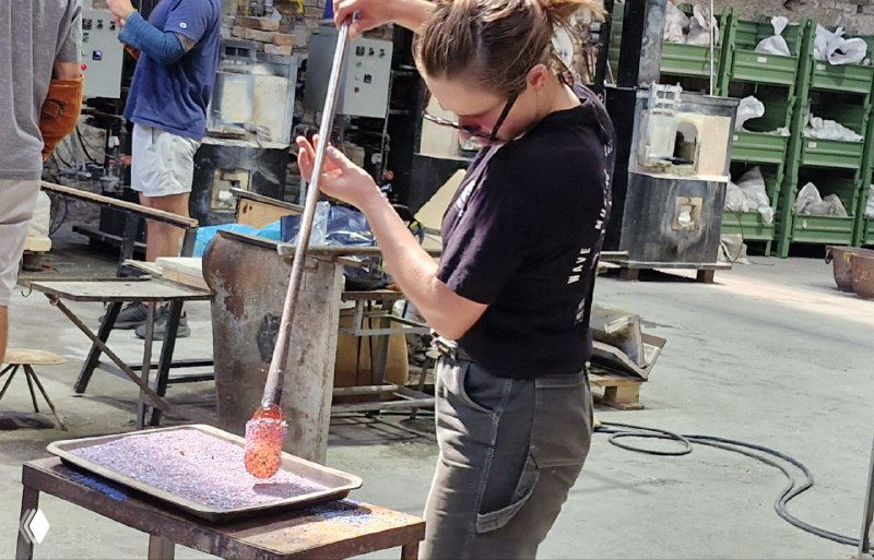 Мастер выдувает изделие, держит трубку над формой в мастерской Мурано — этап придания первоначальной формы стеклянной заготовке.