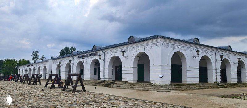 Белокаменные торговые ряды с арочными проходами и мощёной площадью перед ними — историческая торговая зона в одном из подмосковных городков.