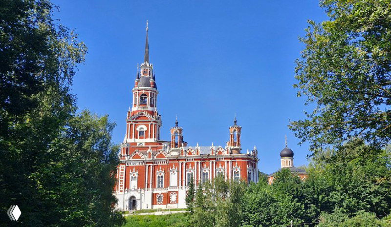 Высокая красочно расписанная церковь на фоне голубого неба и зелёной листвы — архитектурный акцент исторического города в Подмосковье.