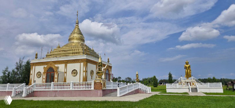 Белый буддийский ступа-пагода и золотая статуя на зелёной лужайке — один из экспонатов этнопарка, отражающий буддийскую архитектуру.