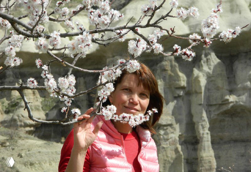 Человек среди ветвей цветущего миндаля на фоне светлых туфовых утёсов Каппадокии — весенний портрет у тропы.