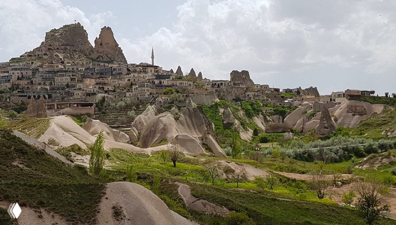 Панорама Учхисара и окружающих туфовых куполов и долин, мягкие контуры ландшафта и аккуратные зелёные участки.