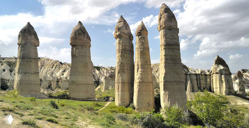 Группа высоких фейри-чимни на фоне мягкой зелени и тропы; вид, характерный для ландшафта долины Любви в Каппадокии.