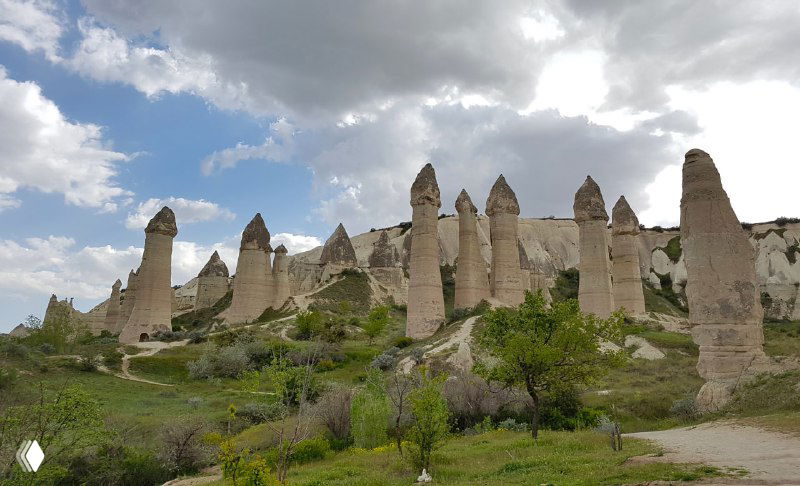 Широкий вид на несколько фейри-чимни и травянистые склоны, по низу которых виднеется пешеходная тропа к Гёреме.