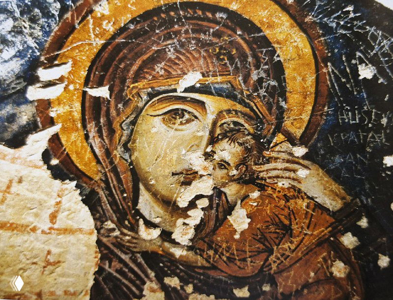 Крупный план повреждённой фрески Богородицы: облупившаяся краска, потертости и следы времени на лицах и орнаменте стены.