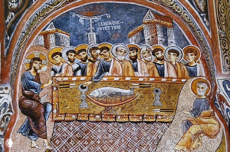 Фреска с религиозной сценой, напоминающая общую трапезу или Тайную вечерю; стол, фигуры апостолов и сложный орнамент внутри церкви.