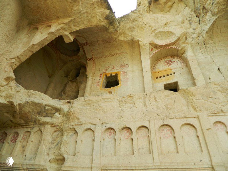 Фрагмент внешней стены и ниши пещерного жилища возле Гёреме: вырезанные в туфе окна, арки и следы старинной архитектуры на скале.