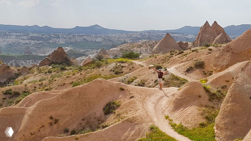 Пешеходная тропа по светло-персиковым скалам Каппадокии, холмы и характерные скальные формы, вдали виднеется панорама долины.