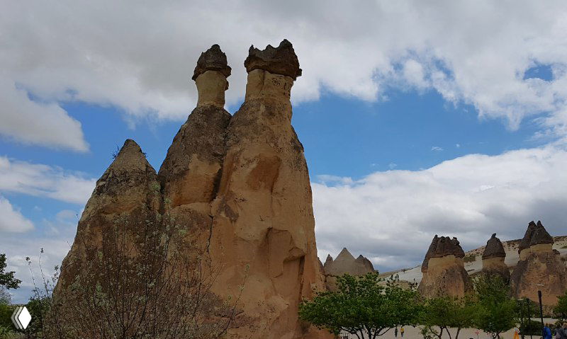Крупный план двухнаправленных скальных форм с «шляпками» на вершинах, панорамный вид на долину и драматичное облачное небо.