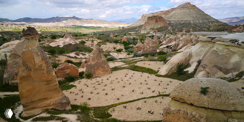 Крупный план вытянутого камня-столба на фоне долины и далекого холма, видны округлые формы и слоистая структура породы.