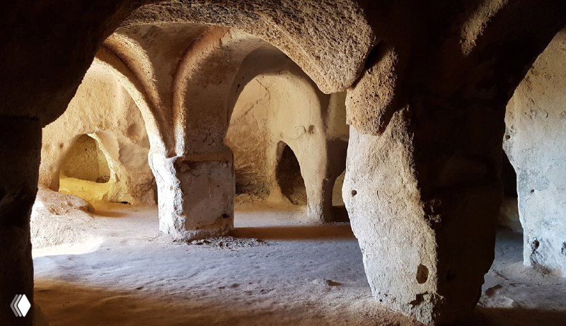 Просторный зал в пещерном комплексе с колоннами и арками, пустые помещения и разноуровневые проходы, характерные для монастырских построек IX века.