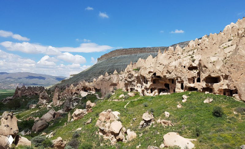 Скальные фасады Зельве с множеством входов и маленькими отверстиями для голубятен, внизу растёт травянистая растительность на склонах.