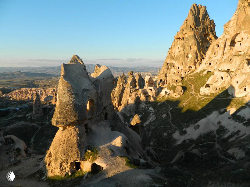 Изрезанные туфовые образования вблизи Учхисара: естественные арки и вырубленные в скале оконные проёмы под голубым небом.
