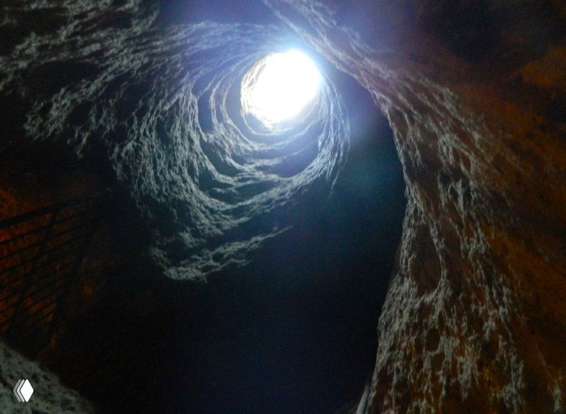 Вертикальная шахта-колодец в подземелье, свет сверху, вид на стены туфа и ступени — элемент вентиляции и доступа к уровням Деринкую.