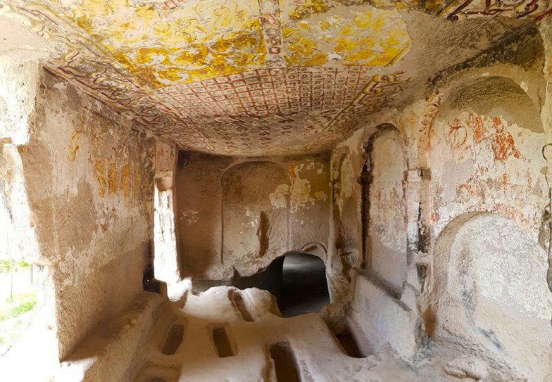 Интерьер одной из пещерных церквей Кешлик: пространство в туфе с потолочными фресками и боковыми нишами, мягкий дневной свет проникает через отверстия.