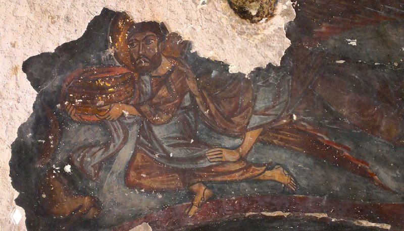 Фрагмент настенной живописи в пещерной церкви Кешлик: фигуры святых и бо́льшие участки сцены с утратами краски и следами времени на поверхности фрески.