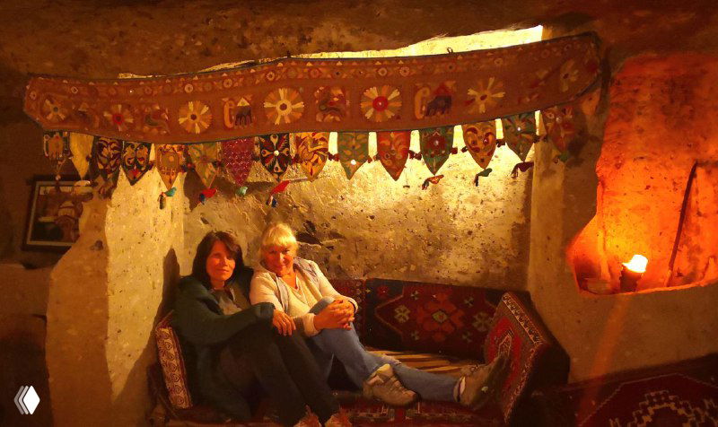 Интерьер пещерного отеля: гости у камина в уютной комнате с традиционными текстилями и мягким освещением.