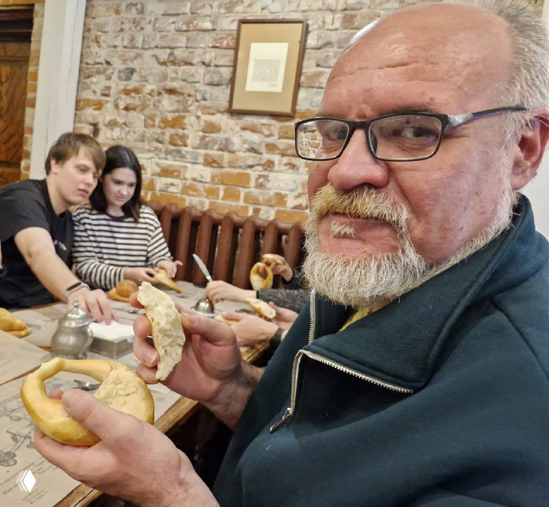 Посетители дегустируют свежие калачи за столом: люди держат булочные изделия и пробуют начинку в уютной лавочке-музее