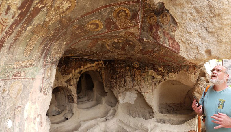 Широкая пещерная ниша с фрагментами росписи на потолке и прогулочный турист рядом для масштаба внутреннего пространства