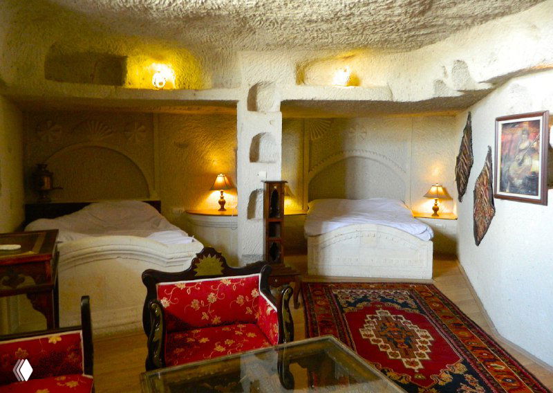 Интерьер пещерного номера с двумя кроватями, традиционными коврами и мягким тёплым освещением, пример размещения в отеле-пещере.