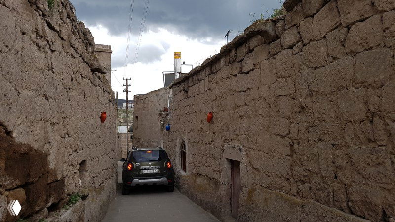 Узкая глиняная улица Каппадокии, где автомобиль почти застрял между плотными стенами домов — пример очень узких дорог региона.