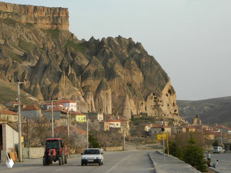 Дорога в Каппадокии мимо скалистых склонов и деревни, вид с шоссе — характерный ландшафт региона и сельская трасса.