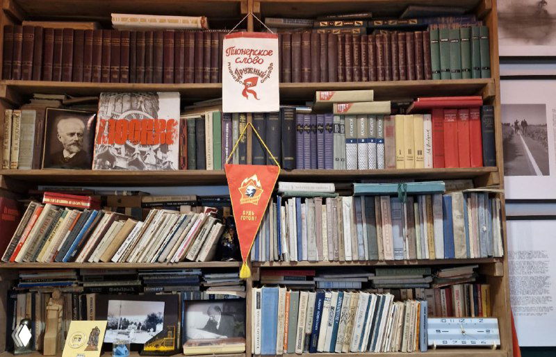 Книжные полки и советские атрибуты в зале «Арткоммуналки»: книги, вымпел и предметы быта прошлых десятилетий на стенах