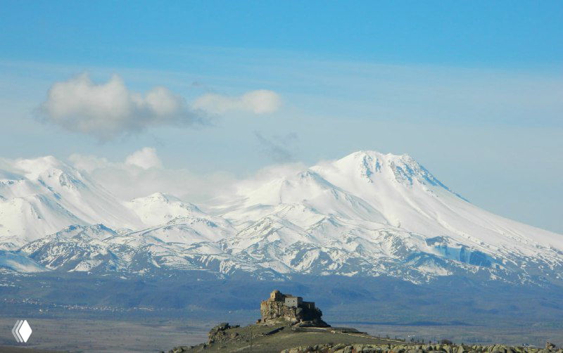 Заснеженная гора и маленькая скальная крепость на переднем плане; вид на горный массив рядом с Каппадокией, снято издалека.