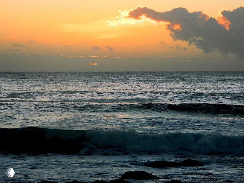 Спокойный океан на фоне залитого красками заката: темные волны на переднем плане и облачное небо, переходящее в золотые тона.