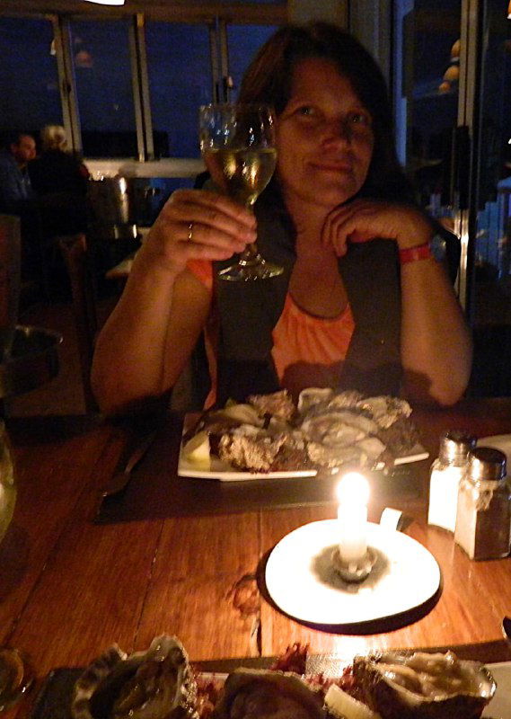 Автор за столиком в ресторане подаёт бокал вина: свеча, тарелка с мидиями и уютная тёплая атмосфера вечернего ужина у океана.