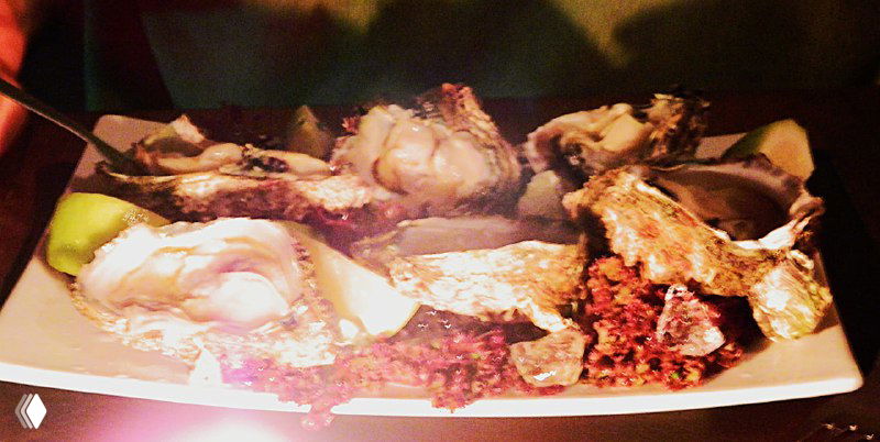 Крупный план тарелки с мидиями и соусами: блюдо на деревянной поверхности при тёплом свете, аппетитный вид морепродуктов.