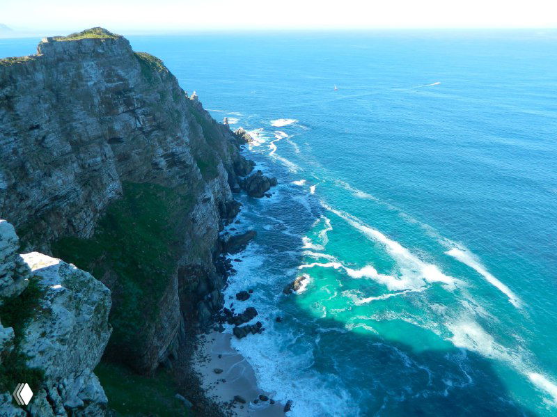 Крутые прибрежные скалы и узкие пляжные участки, изрезанный берег и бирюзовые заливы в ясный день около Кейптауна.