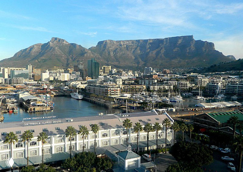 Панорамный вид на набережную, здания и Столовую гору; портовая зона и городской силуэт у воды при дневном освещении.