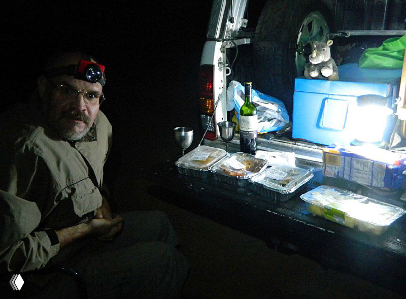Ночная стоянка на обочине: открытый багажник автомобиля, фонарик, рассортированная еда и снаряжение — сцена кемпинга перед поездкой в Намибию.