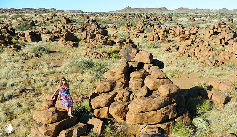 Человек прогуливается между округлыми и прямоугольными камнями на фоне каменистого ландшафта «Игровой площадки великанов», подчёркивая масштаб глыб.