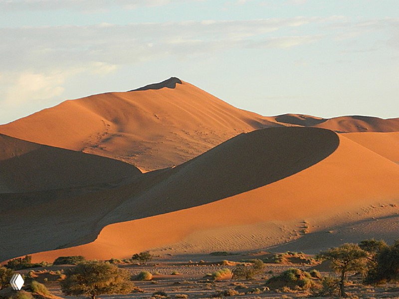 Крупный план изогнутой оранжево-красной дюны Соссусфлей с глубокими тенями и выступающим гребнем под вечерним небом.