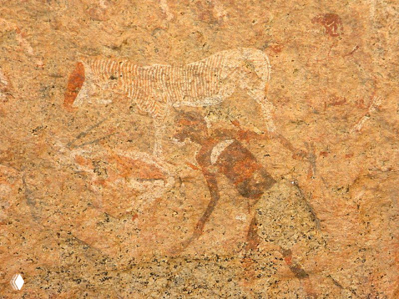 Изображение животного и человеческой фигуры на скале: очертания тела, локальные потертости краски и текстура скальной поверхности видны крупно.